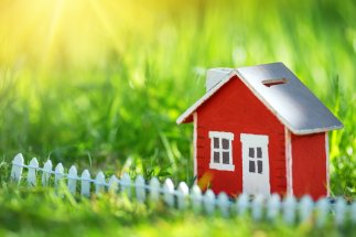 Rotes Miniaturhaus mit kleinem weißen Zaun im hohen grünen Gras