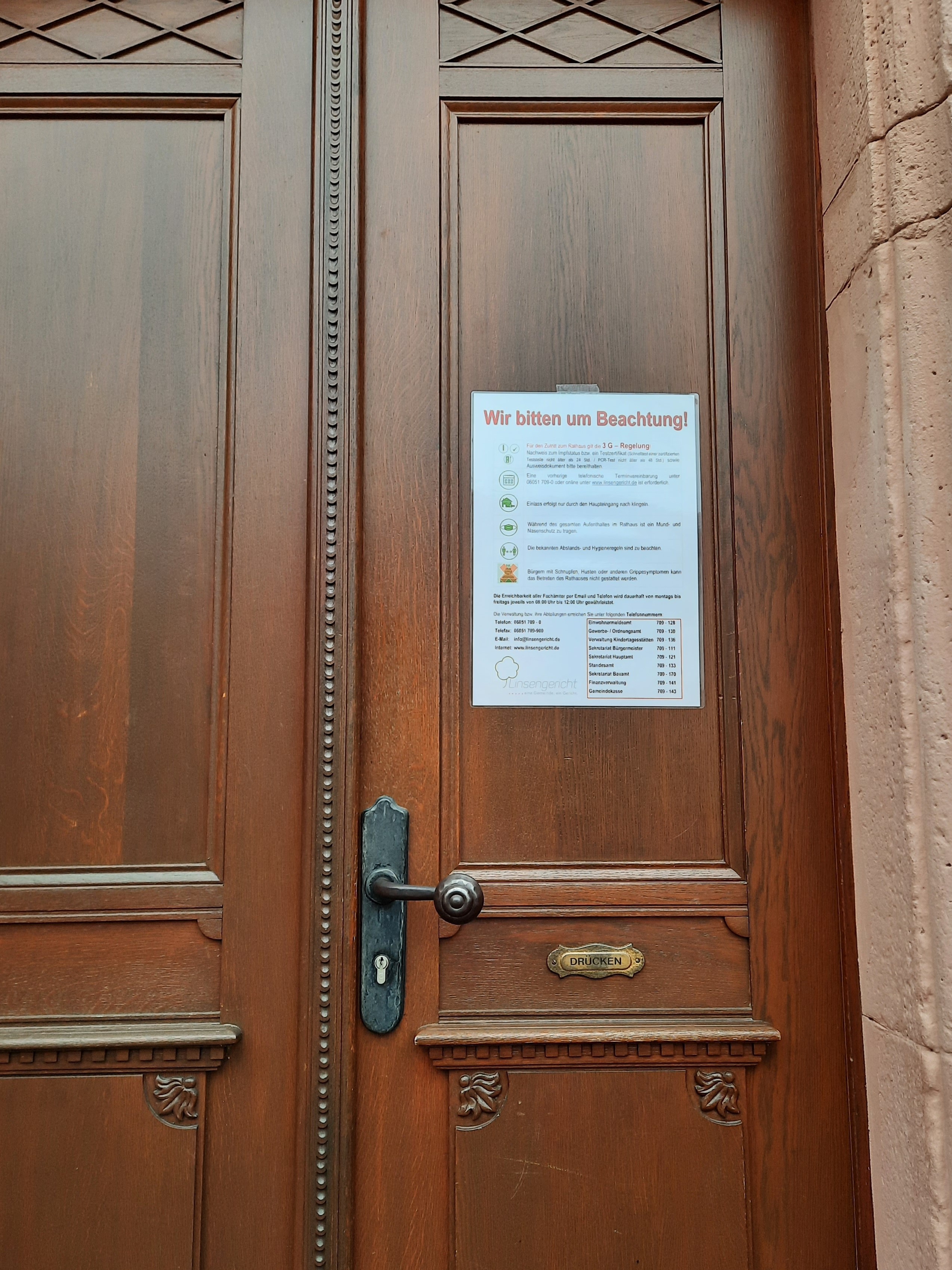 HInweisschild an brauner Holz-Eingangstür des Rathauses Linsengericht mit den Hinweisen zur 3G-Regelung