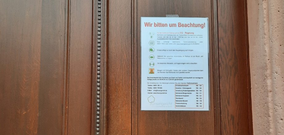 HInweisschild an brauner Holz-Eingangstür des Rathauses Linsengericht mit den Hinweisen zur 3G-Regelung