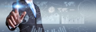 Digitalisierung Mann im Anzug tippt von hinten gegen eine durchsichtige Fläche auf der in weißer Farbe verschieden Symbole, Diagramme und achteckige Formen angeordnet sind.