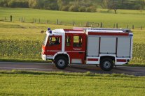 Ein Katastrophenschutzfahrzeug des Landes Hessen auf einer Landstraße, umgeben von grünen Wiesen und Feldern.