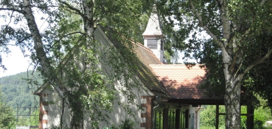 Trauerhalle am Friedhof im Ortsteil Eidengesäß, umgeben von Bäumen. Im Vordergrund ist der Eingangsbereich zum Friedhof zu erkennen.