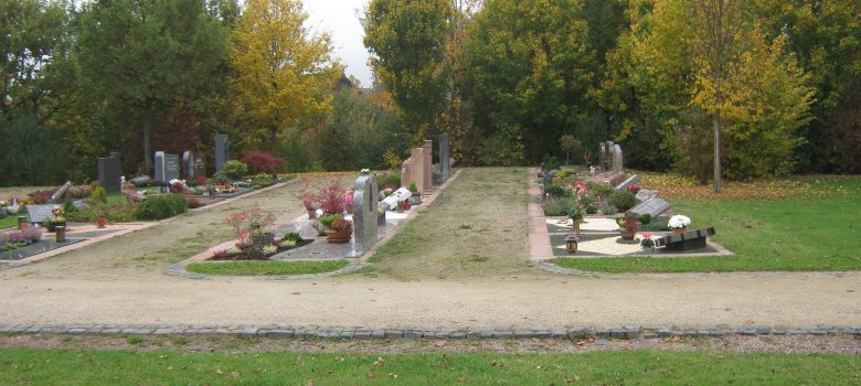 Drei Reihen von Doppelgräbern mit dazwischen liegenden Kieswegen. Im rechten Bildbereich sind freie Grünflächen erkennbar.