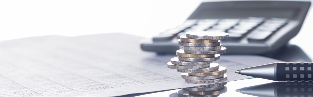 Münzstapel auf einem Blatt mit einer Tabelle, mit Stift und Taschenrechner