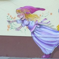 Die Lustige Wandbemalung der Kita zeigt ein Zwergenmädchen mit Blumen in der Hand