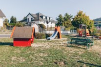 Spielplatz in Geislitz mit Spielhaus, Rutsche und Sitzmöglichkeiten im Vordergrund