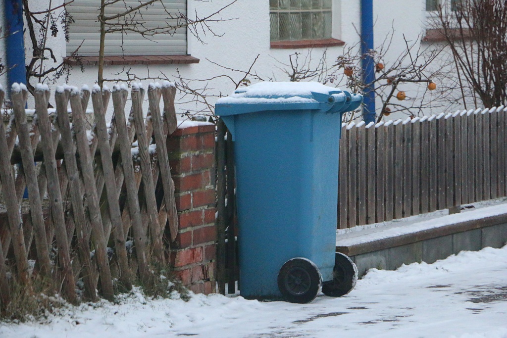 blue plastic recycling bin for paper waste stands at the roadside, covered in snow, ready for collection blue plastic recycling bin for paper waste stands at the roadside, covered in snow, ready for collection