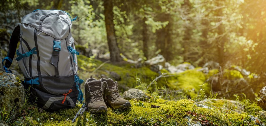 Rucksack, Wanderschuhe, Wanderstöcke auf Waldboden abgestellt