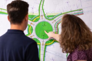 Mitarbeiterin deutet mit Finger auf eine Planskizze, um dem Kollegen etwas zu visualisieren