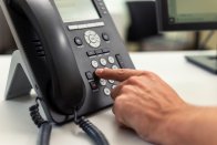 Person drückt Taste auf einem stationären Telefon