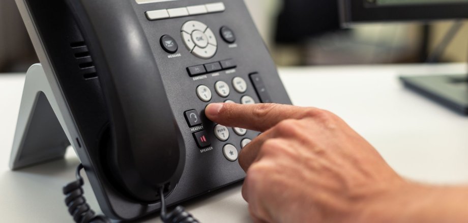 Person drückt Taste auf einem stationären Telefon