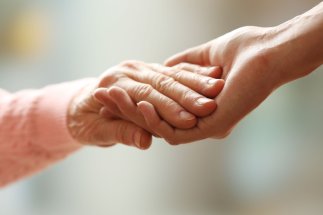 Nahaufnahme einer alten und einer jungen Hand, die einander umfassen