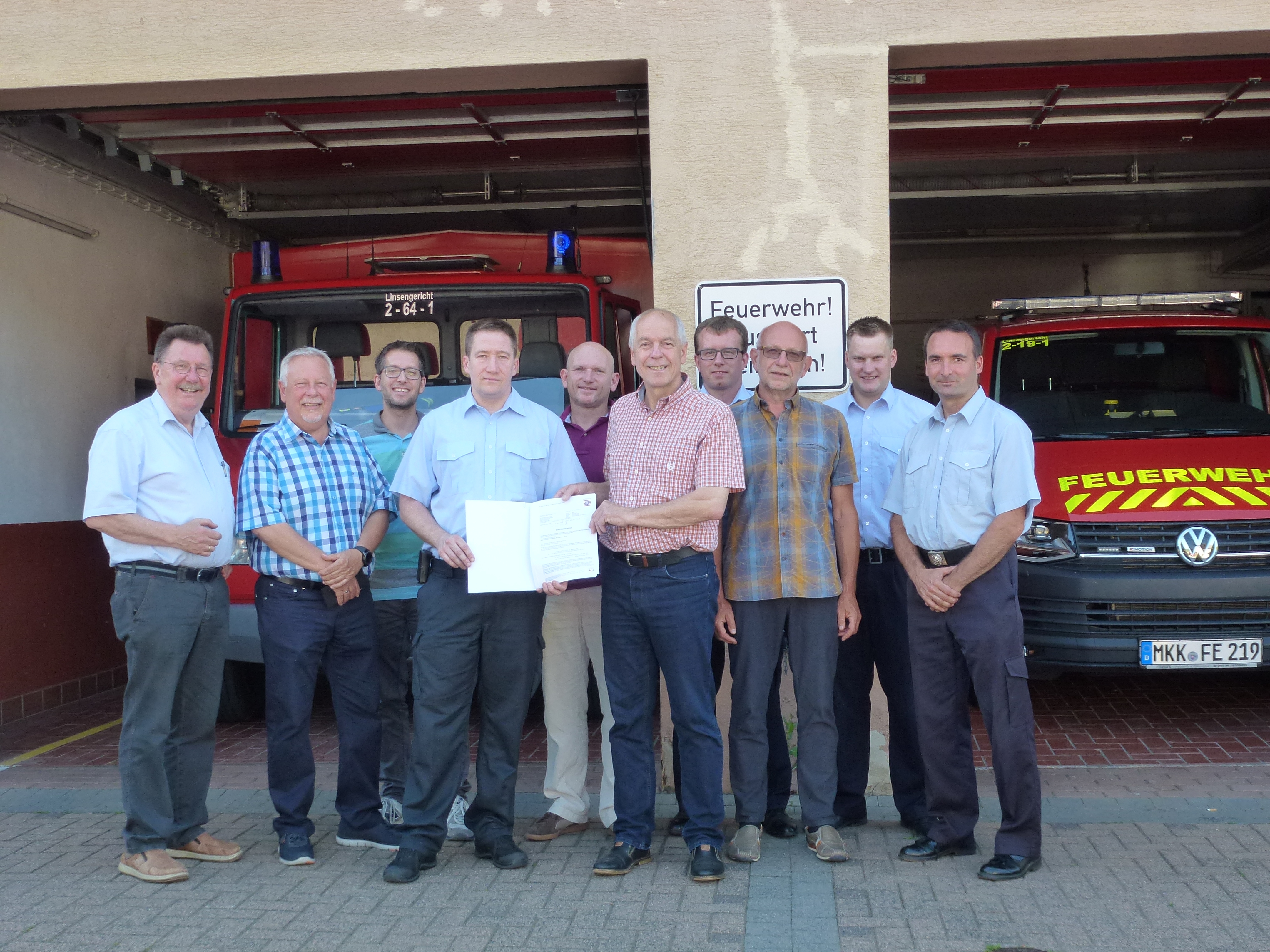 Vor der geöffneten Fahrzeughalle des Feuerwehrhauses Eidengesäß stehen mehrere Personen und halten den Zuwendungsbescheid in der Hand.