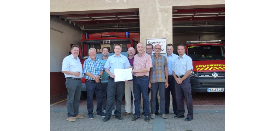 Vor der geöffneten Fahrzeughalle des Feuerwehrhauses Eidengesäß stehen mehrere Personen und halten den Zuwendungsbescheid in der Hand.