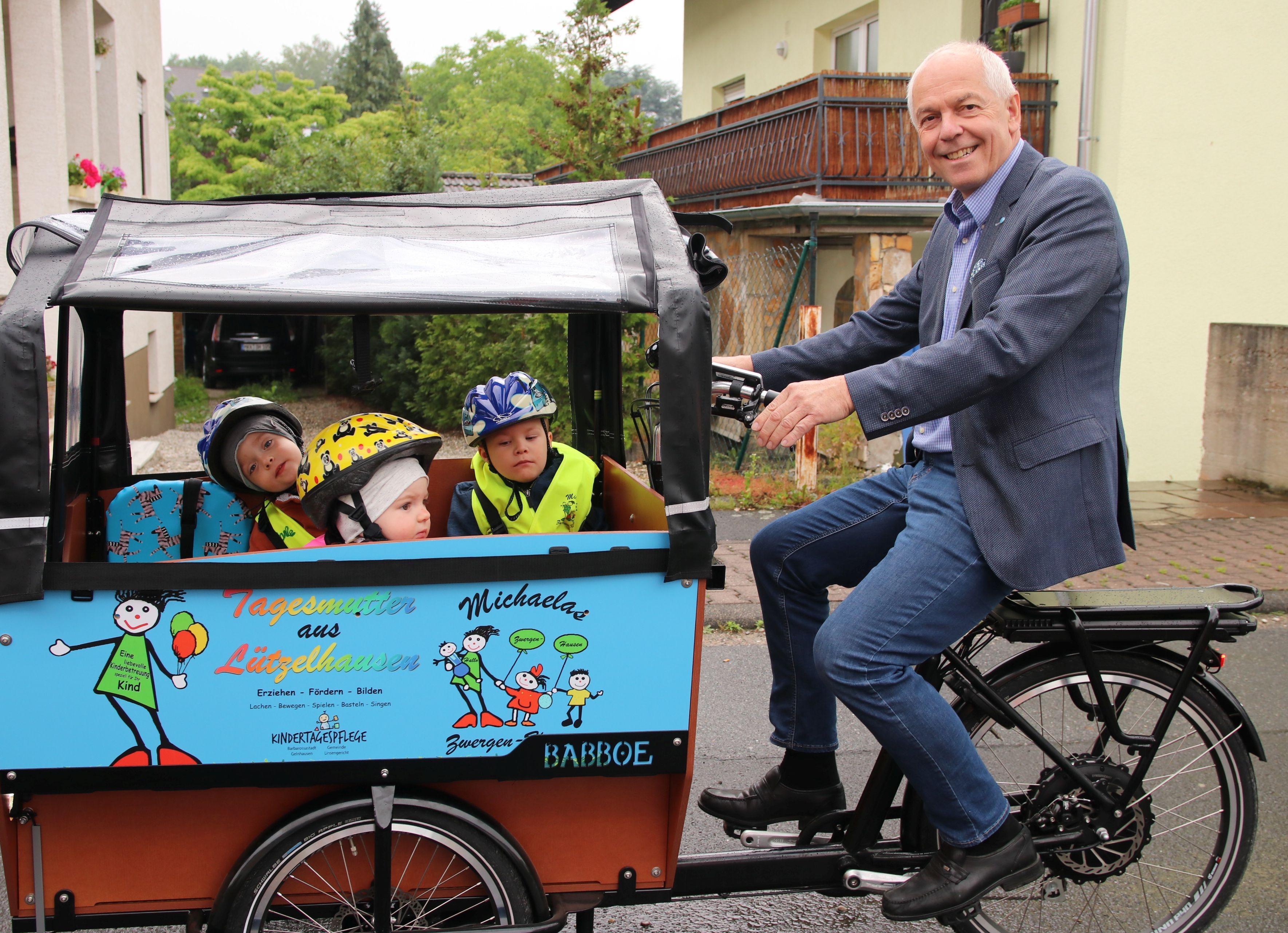 Bürgermeister Albert Ungermann sitzt auf einem Lastenfahrrad in dessen Anhänger Kinder sitzen.