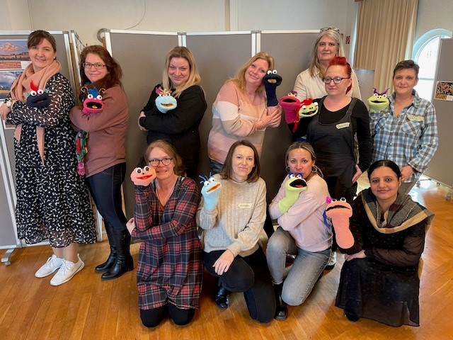 11 Personen mit Handpuppen vor einer Stellwand