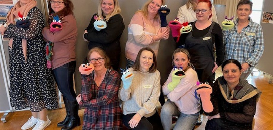 11 Personen mit Handpuppen vor einer Stellwand