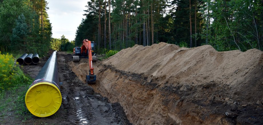 Excavator digging trench in ground for laying pipeline of natural gas. Building of transit petrochemical pipe in forest area. Carry diluted bitumen and crude to international markets. Oil and gas