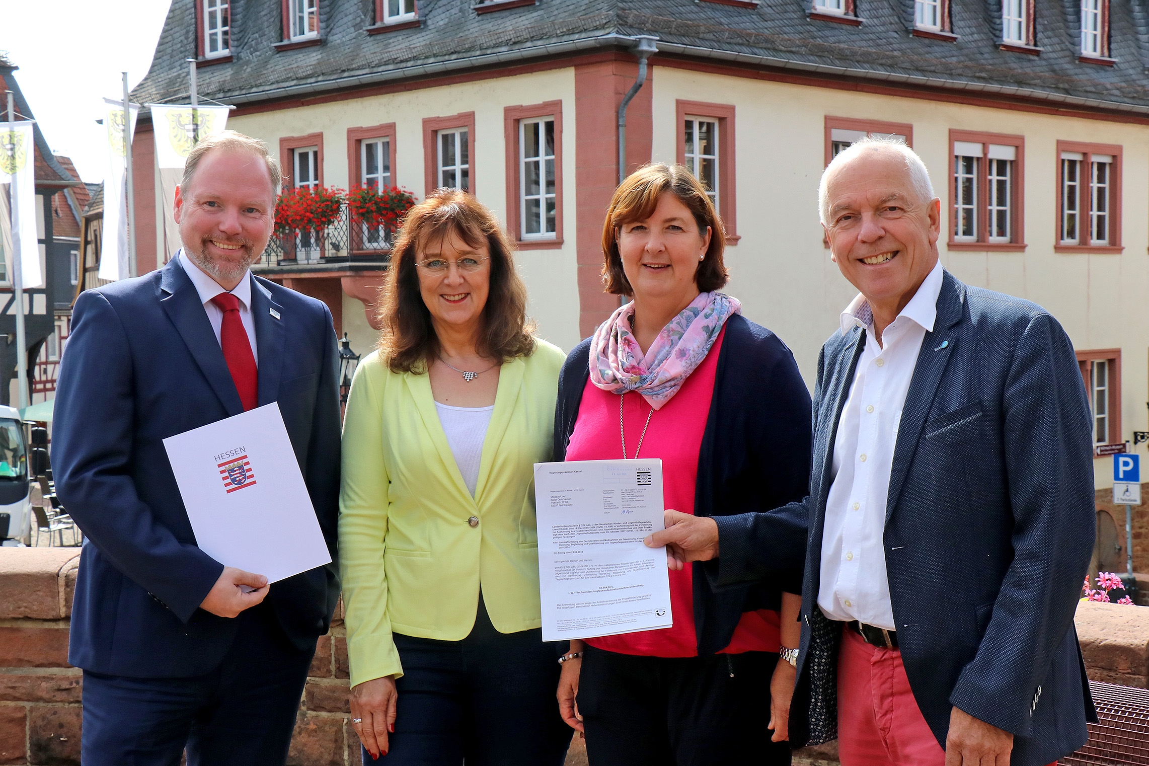 Vier Personen mit Schriftstücken in den Händen vor Gebäuden