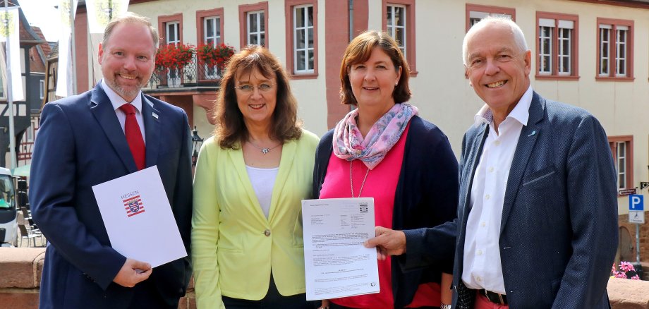 Vier Personen mit Schriftstücken in den Händen vor Gebäuden