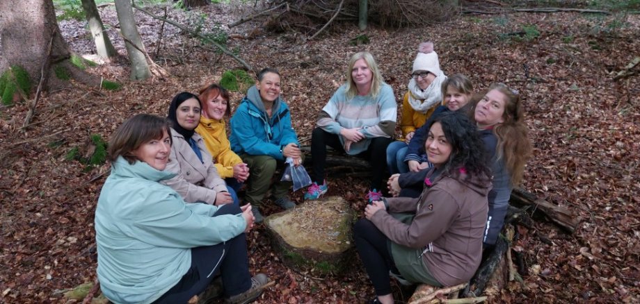 Kindertagespflegepersonen sitzen im Kreis auf Waldboden