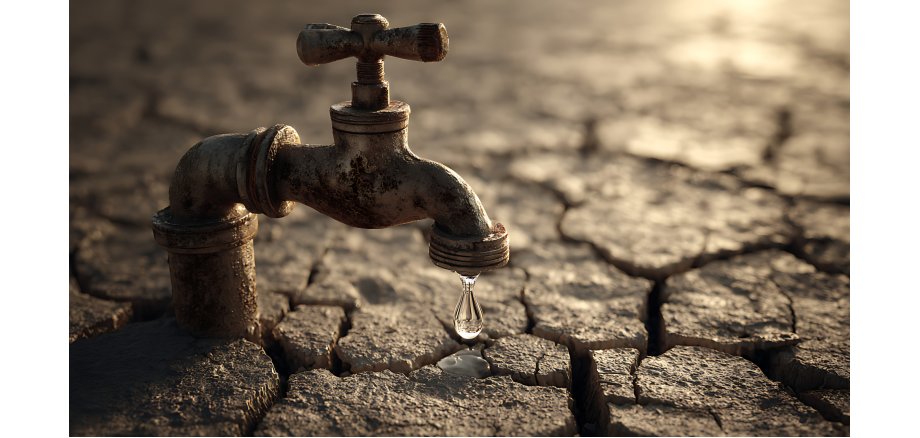 Leaking faucet on cracked earth symbolizes water scarcity and drought conditions.